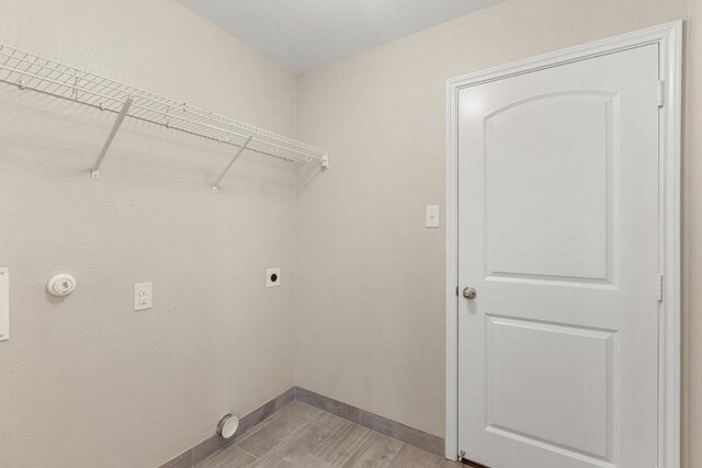 clothes washing area featuring light wood-style floors, baseboards, hookup for an electric dryer, and laundry area