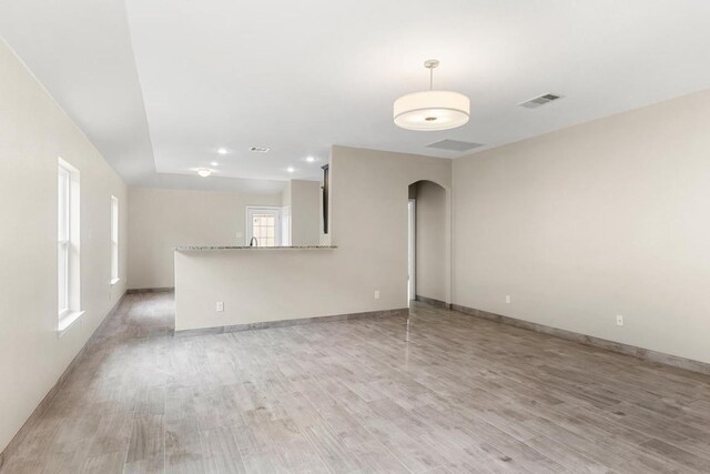 unfurnished living room featuring light wood-style floors, arched walkways, and baseboards