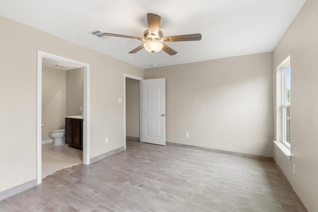 unfurnished bedroom featuring connected bathroom, baseboards, multiple windows, and light wood-type flooring