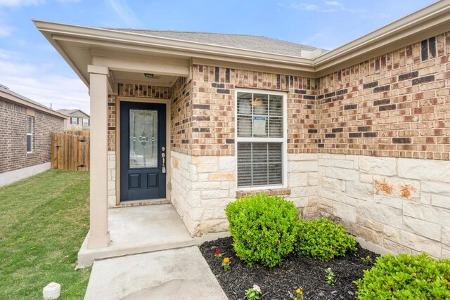 property entrance featuring fence, a yard, and stone siding