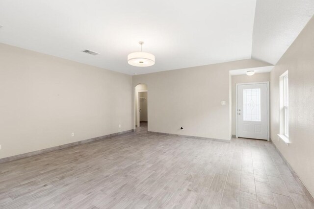 spare room with visible vents, lofted ceiling, baseboards, arched walkways, and light wood finished floors