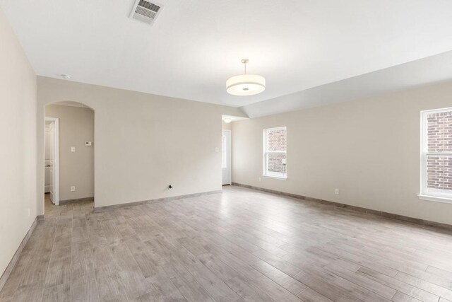 empty room featuring arched walkways, baseboards, light wood finished floors, and visible vents