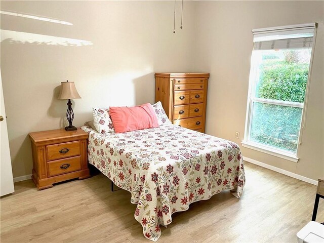 bedroom with baseboards, multiple windows, and light wood-type flooring