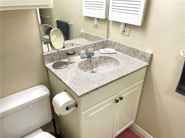 half bathroom with toilet, a textured wall, and vanity
