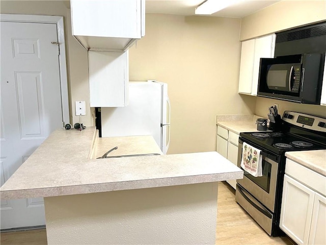 kitchen with black microwave, stainless steel electric range oven, light countertops, freestanding refrigerator, and a peninsula