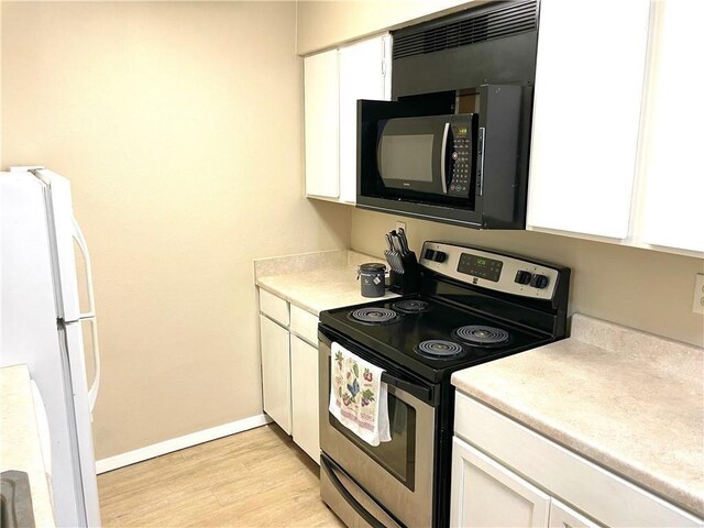 kitchen with electric stove, white cabinetry, black microwave, and freestanding refrigerator