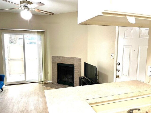 living room featuring a ceiling fan, wood finished floors, and a brick fireplace