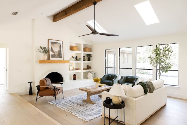living area with light wood-style floors, baseboards, a skylight, and beamed ceiling