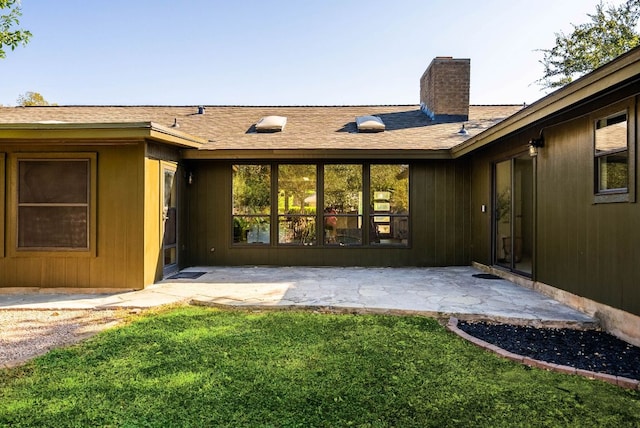 back of property with a lawn, a chimney, a shingled roof, and a patio area