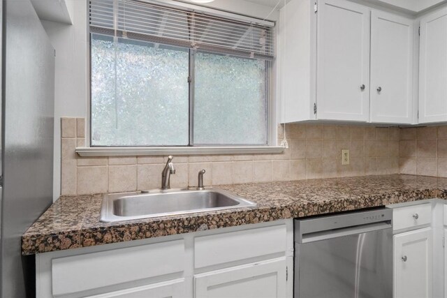 kitchen with decorative backsplash, dark countertops, dishwasher, a sink, and white cabinets