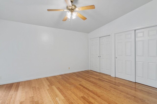 unfurnished bedroom featuring a ceiling fan, vaulted ceiling, baseboards, light wood finished floors, and multiple closets