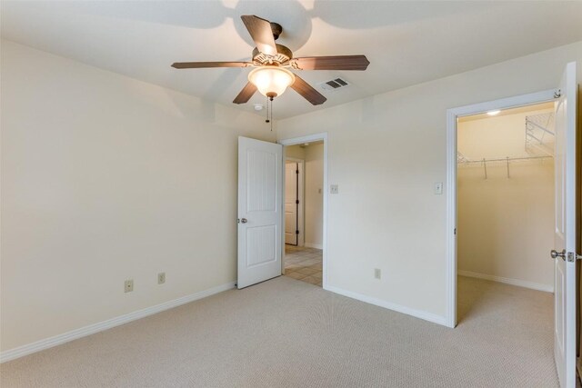 unfurnished bedroom featuring visible vents, baseboards, a walk in closet, ceiling fan, and light colored carpet