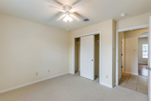 unfurnished bedroom featuring visible vents, a closet, light carpet, baseboards, and arched walkways