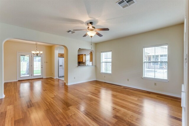 unfurnished living room with light wood-style floors, arched walkways, ceiling fan with notable chandelier, and visible vents