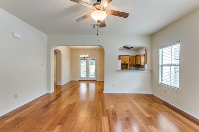 unfurnished living room with arched walkways, light wood-style flooring, ceiling fan with notable chandelier, baseboards, and visible vents