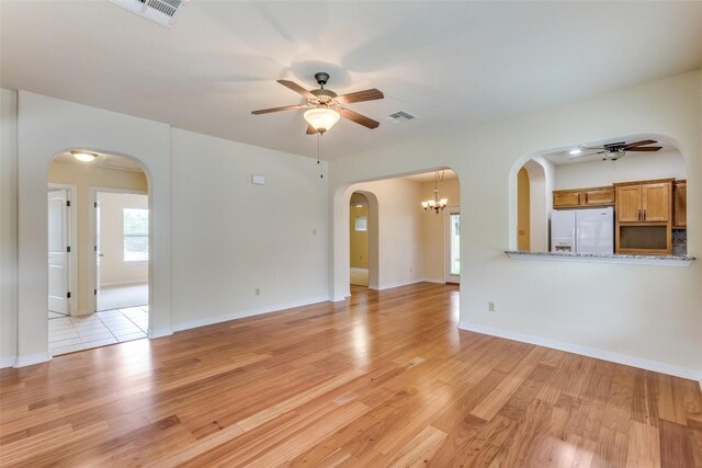 unfurnished living room featuring arched walkways, ceiling fan with notable chandelier, light wood-type flooring, and visible vents