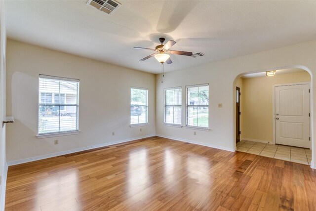 empty room with arched walkways, a ceiling fan, visible vents, and light wood-style flooring