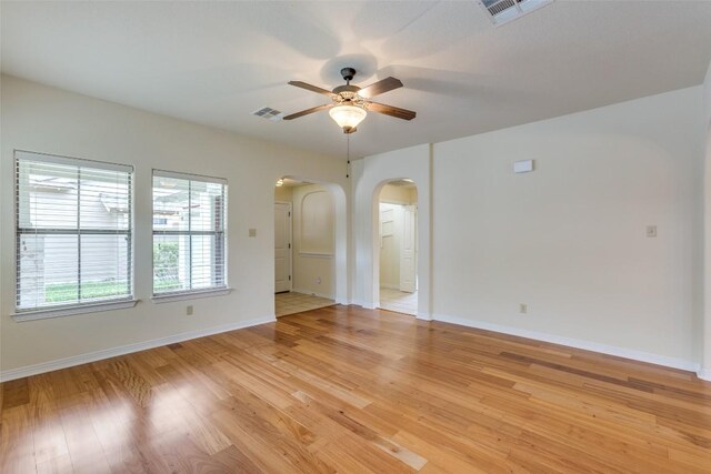 empty room with arched walkways, a ceiling fan, visible vents, and light wood finished floors
