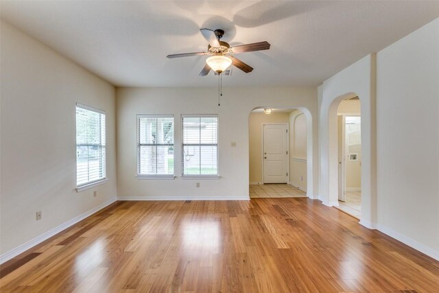 spare room with a ceiling fan, arched walkways, baseboards, and light wood-style floors