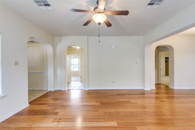 spare room featuring light wood-style floors, arched walkways, ceiling fan, and visible vents