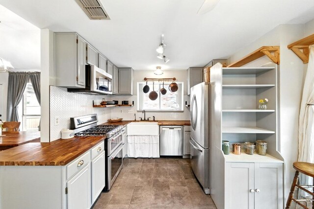 kitchen featuring visible vents, open shelves, butcher block counters, tasteful backsplash, and stainless steel appliances