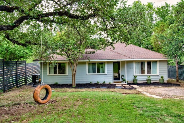 ranch-style house with fence, roof with shingles, central AC, and a front lawn