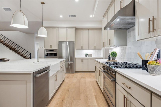 kitchen with a sink, light wood-style floors, stainless steel appliances, under cabinet range hood, and visible vents