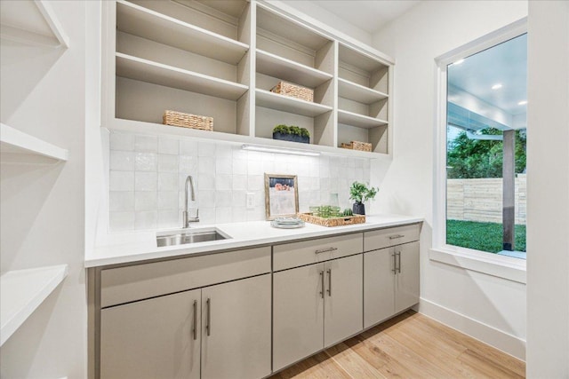 bar featuring baseboards, light wood-type flooring, a sink, and tasteful backsplash