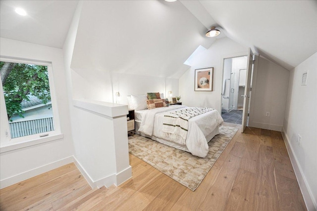 bedroom with connected bathroom, baseboards, vaulted ceiling, and light wood-style floors