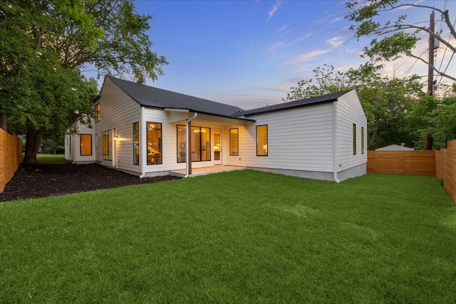 rear view of property with a lawn, a shingled roof, and a fenced backyard