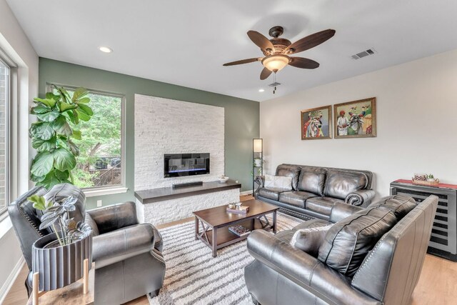 living room featuring visible vents, wood finished floors, a fireplace, baseboards, and a ceiling fan