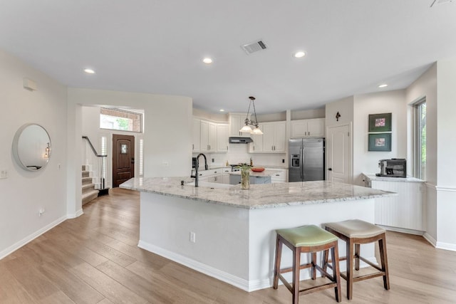 10636 Bramblecrest Dr, Austin, TX 78726 - kitchen with stainless steel fridge, white cabinetry, light wood-style flooring, a kitchen breakfast bar, and recessed lighting
