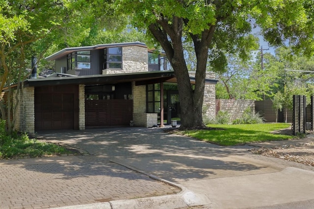 view of front of property with fence, driveway, stone siding, and a garage