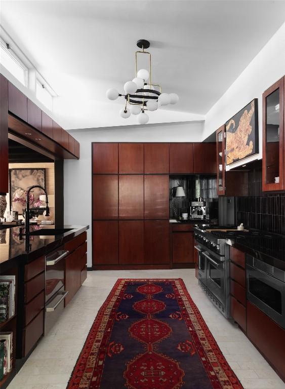kitchen with an inviting chandelier, dark countertops, glass insert cabinets, a sink, and double oven range