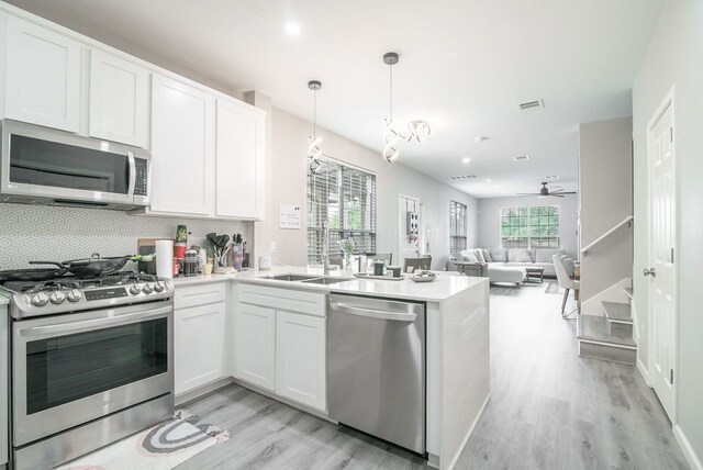 kitchen with visible vents, a peninsula, light wood-type flooring, a sink, and stainless steel appliances