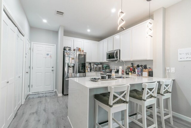 kitchen with light wood-style flooring, a peninsula, a breakfast bar, and stainless steel appliances