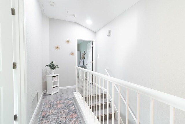 hallway with visible vents, wood finished floors, vaulted ceiling, and an upstairs landing