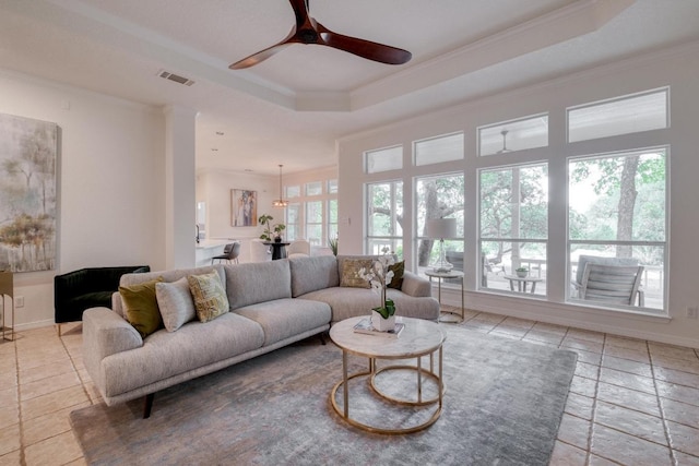 living room with ceiling fan, visible vents, a raised ceiling, baseboards, and ornamental molding