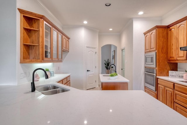kitchen featuring crown molding, appliances with stainless steel finishes, a sink, arched walkways, and a center island