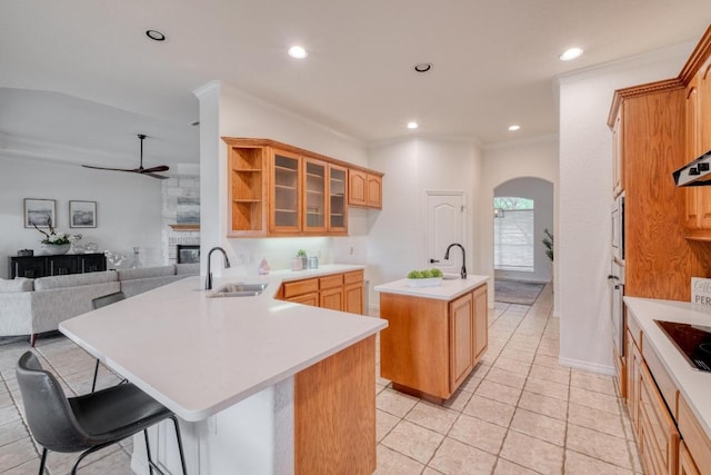 kitchen with ceiling fan, a sink, a kitchen island with sink, arched walkways, and open floor plan