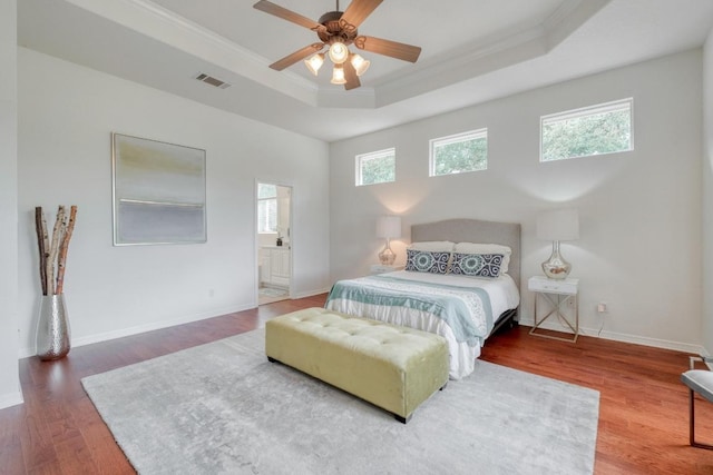 bedroom with visible vents, crown molding, wood finished floors, baseboards, and a tray ceiling
