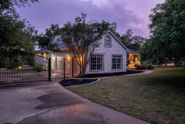 view of front facade featuring a yard, driveway, a gate, and stone siding