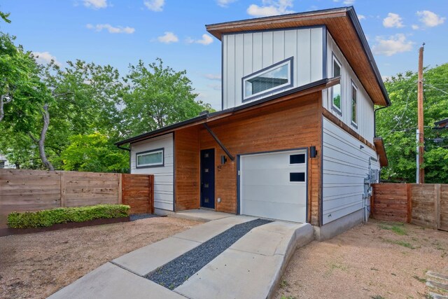 modern home featuring an attached garage, board and batten siding, fence, and concrete driveway