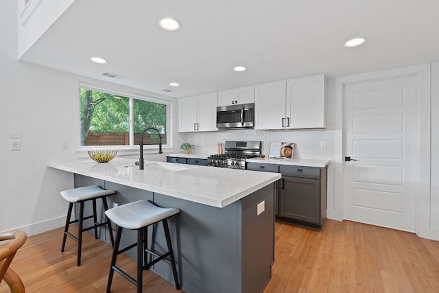 402 W 55th St Unit 2, Austin, TX 78751 - kitchen with stainless steel appliances, a sink, a breakfast bar area, light wood-style floors, and decorative backsplash