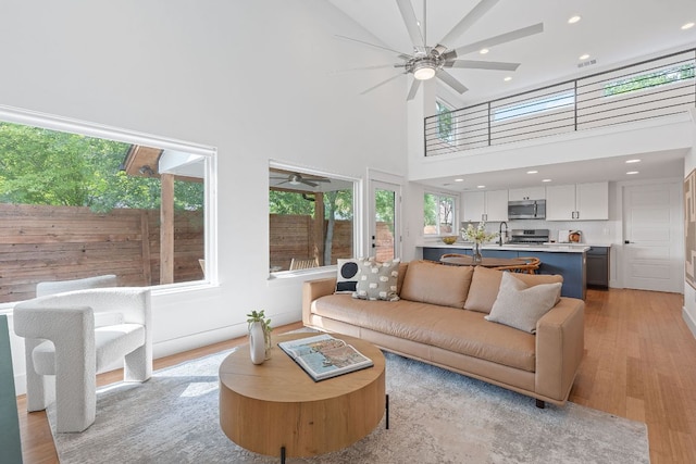 living room featuring light wood-type flooring, recessed lighting, ceiling fan, and a high ceiling