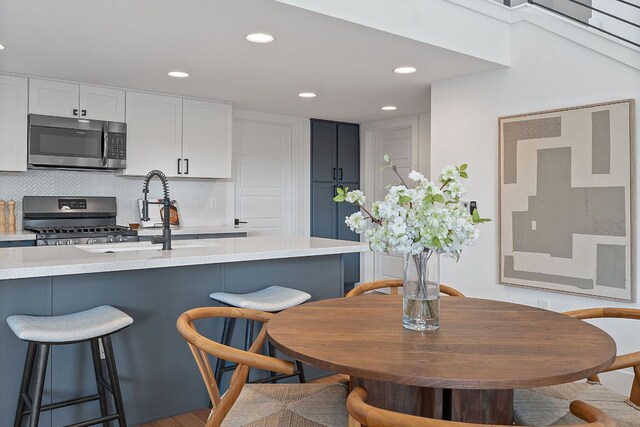 kitchen with appliances with stainless steel finishes, a sink, light countertops, a kitchen breakfast bar, and backsplash