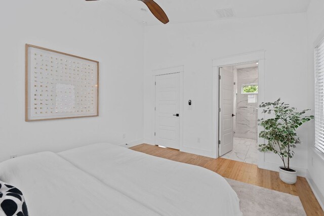 bedroom featuring baseboards, wood finished floors, ensuite bathroom, vaulted ceiling, and visible vents
