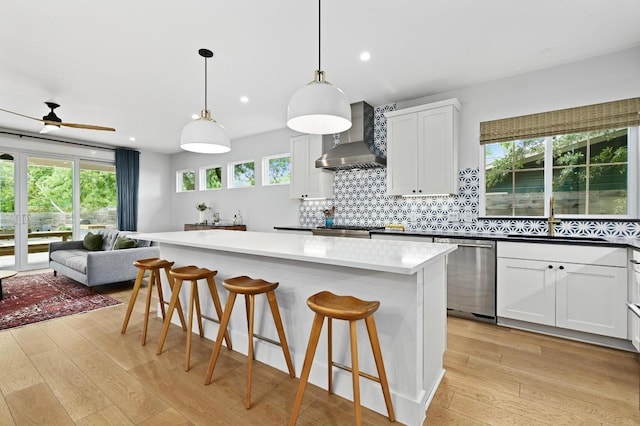kitchen with a sink, light wood-style flooring, wall chimney exhaust hood, and dishwasher