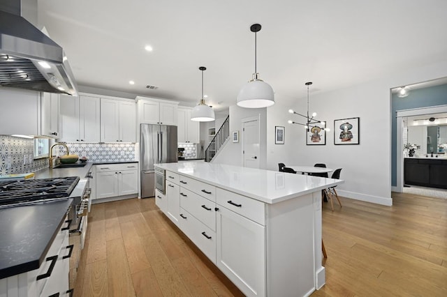 kitchen with wall chimney range hood, light wood finished floors, high end refrigerator, a center island, and backsplash
