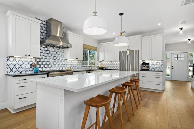 kitchen with visible vents, a kitchen island, light wood-style floors, recessed lighting, and wall chimney exhaust hood